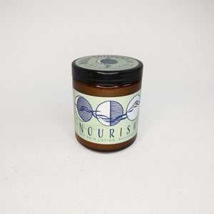 Amber glass jar or "Nourish" Dry skin lotion on a white background. Label has three moons with a willow branch in dark blue on a light green background. 