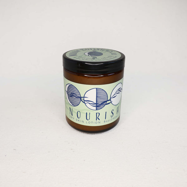 Amber glass jar or "Nourish" Dry skin lotion on a white background. Label has three moons with a willow branch in dark blue on a light green background. 