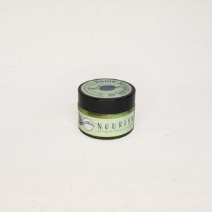 Small green slightly see-through jar of "Nourish" Dry Skin Cream with a black lid on a white background