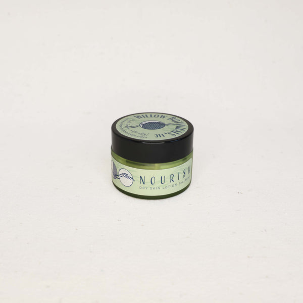 Small green slightly see-through jar of "Nourish" Dry Skin Cream with a black lid on a white background