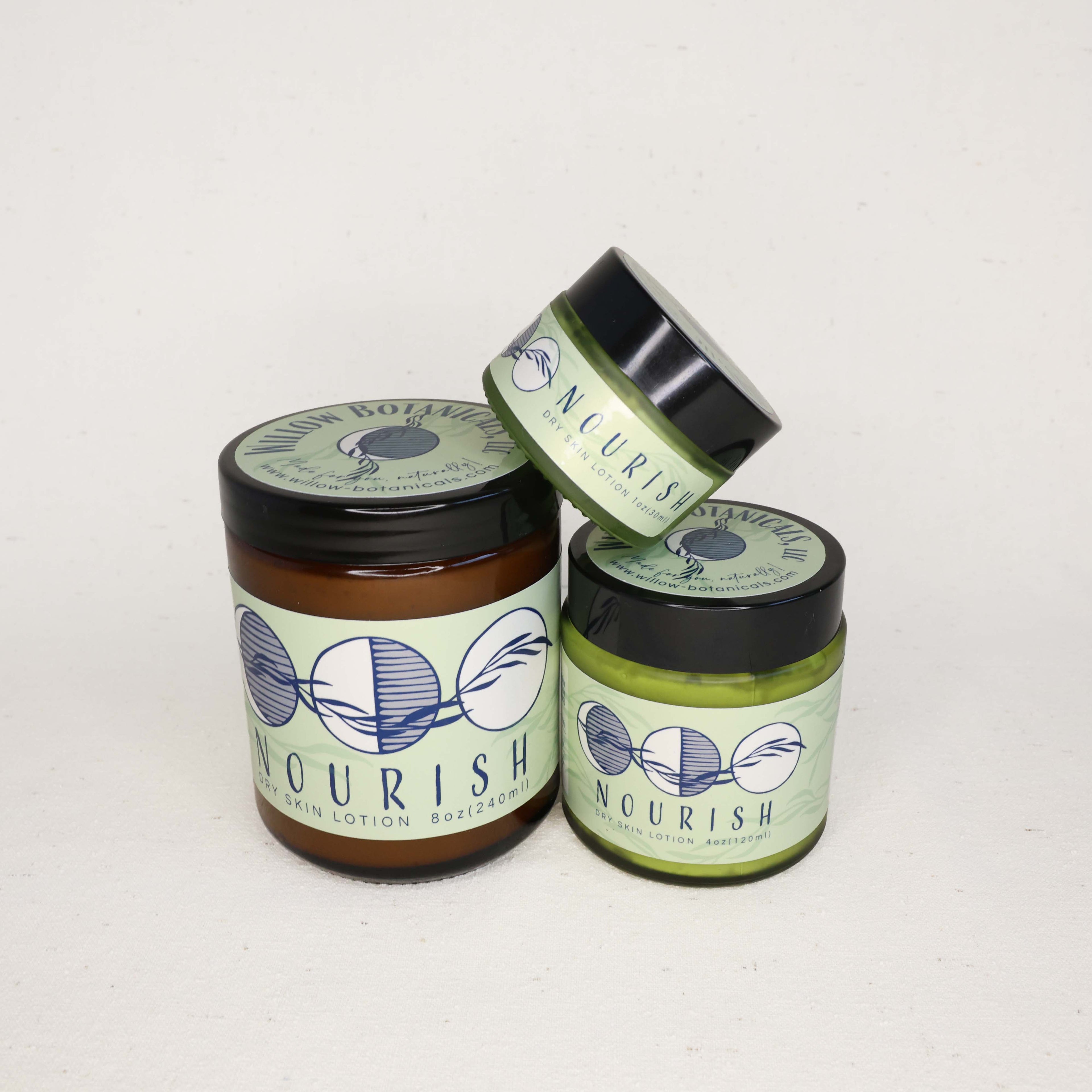Three jars of 'Nourish' Dry skin lotion on a white background. Small jar tilted and balanced on top of the two larger jars.