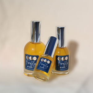 Three bottles of 'Firefly Moon' perfume on a beige background. Center smallest bottle is leaning on two bottles behind.